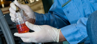 Gloved hands holding bottle of red liquid.